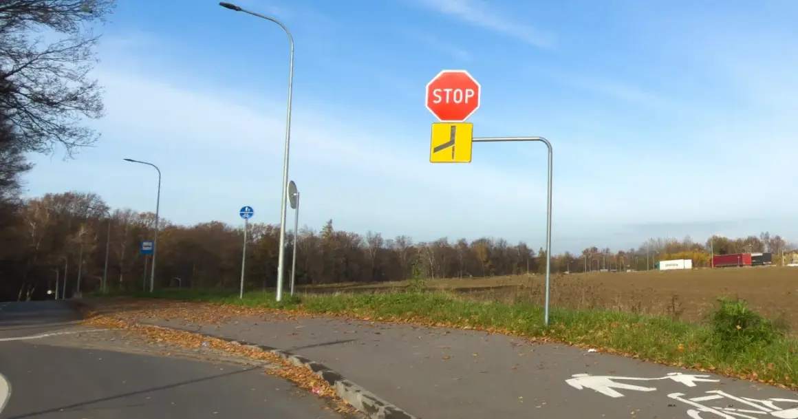 Znak STOP i znak informujący o drodze z pierwszeństwem łamanym. Na ścieżce rowerowej namalowane symbole pieszych i rowerzystów.