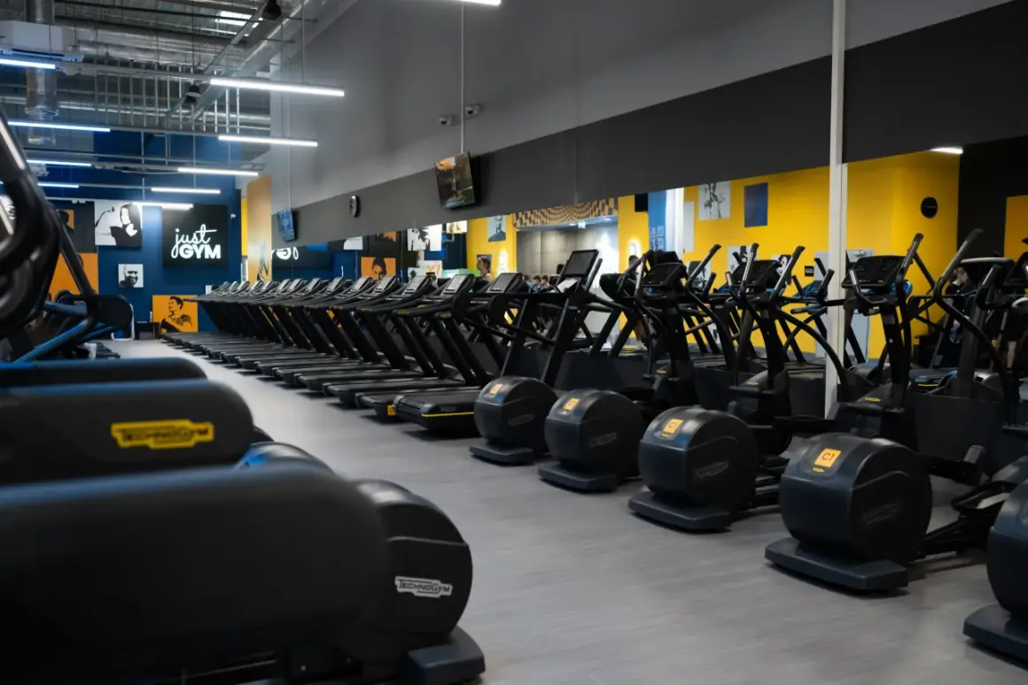 Rzędy bieżni i orbitreków w siłowni Just Gym. Chcesz wiedzieć, jak wejść na Multisport? Tu zaczynasz trening!