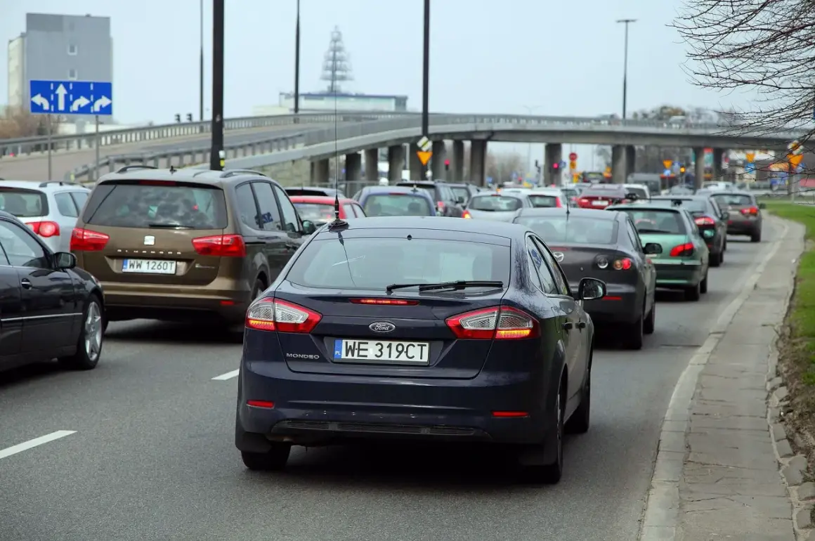 Korki na drodze, kierowcy czekają na zwrot za dojazdy do pracy. Widać rząd samochodów, w tym ciemnogranatowego Forda Mondeo.