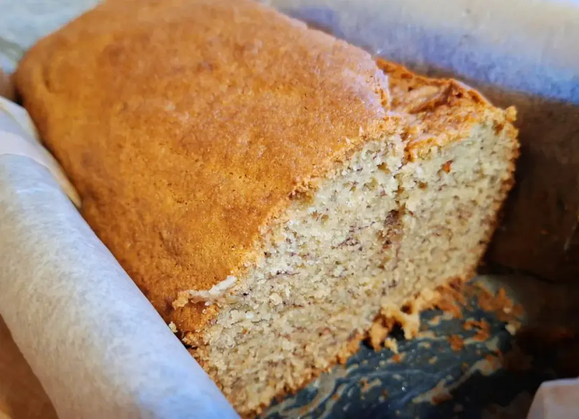 Pyszny, domowy chlebek bananowy w papierowej formie, z widocznymi kawałkami banana w środku.