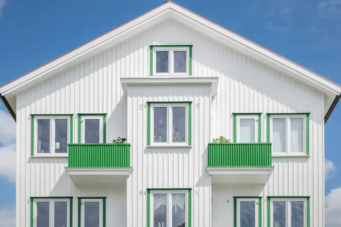 Vitt trähus med gröna detaljer runt fönster och balkonger. Ett perfekt hus att måla om för att fräscha upp.