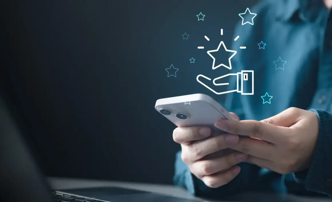 Dłoń trzymająca smartfon z ikoną gwiazdki i dłoni, symbolizującą ocenę.