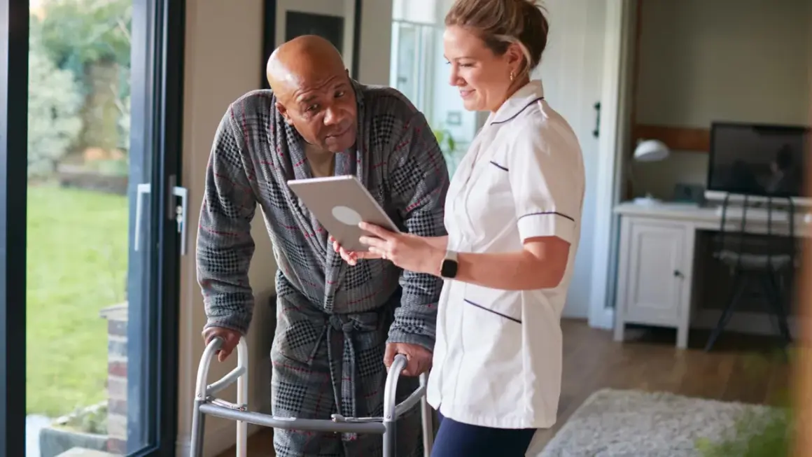 Pflegekraft zeigt Mann mit Gehhilfe auf Tablet, wie oft kann man eine Reha beantragen.