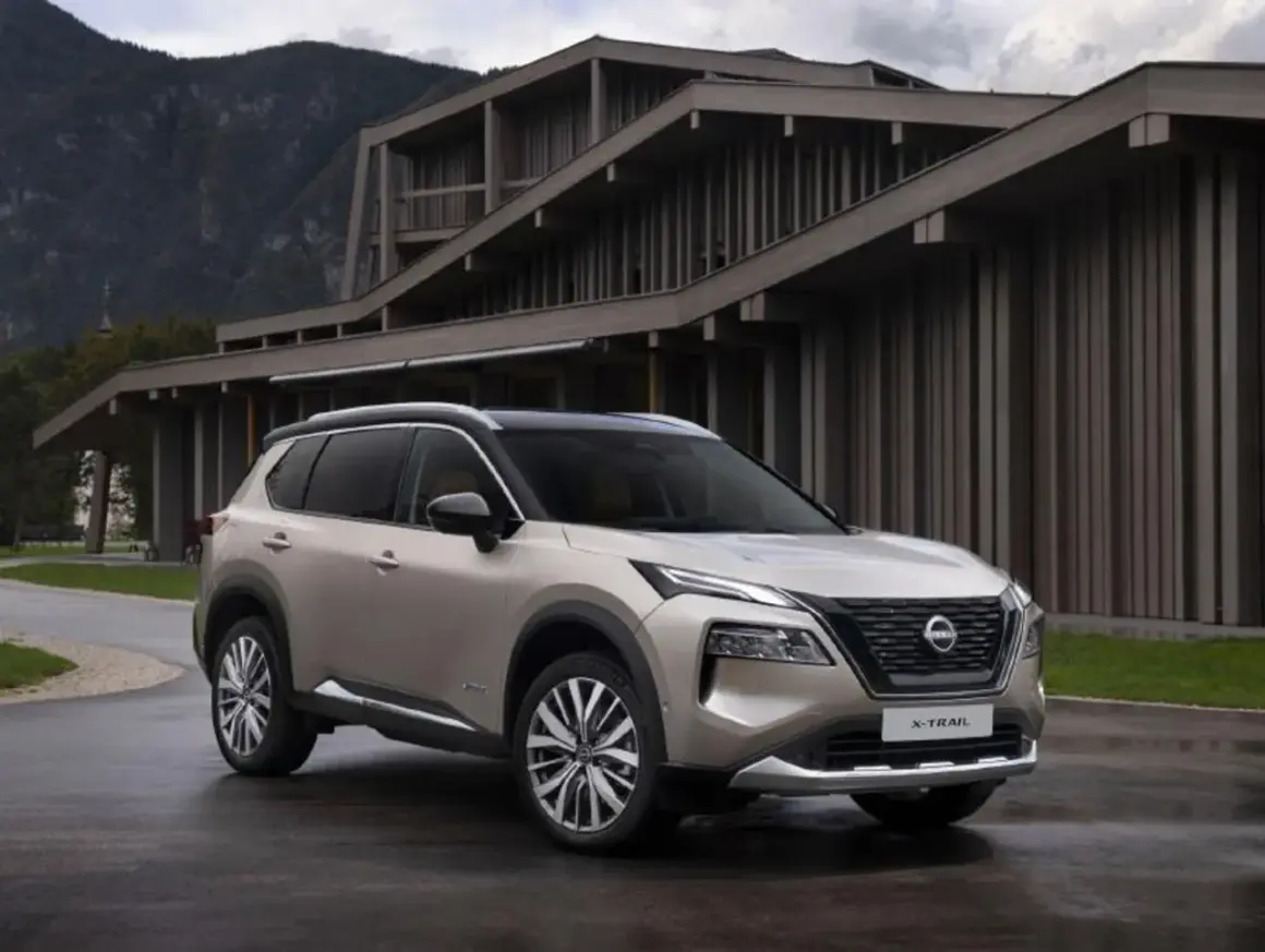 Elegancki, beżowy Nissan X-Trail 2015 zaparkowany przed nowoczesnym budynkiem w górach.