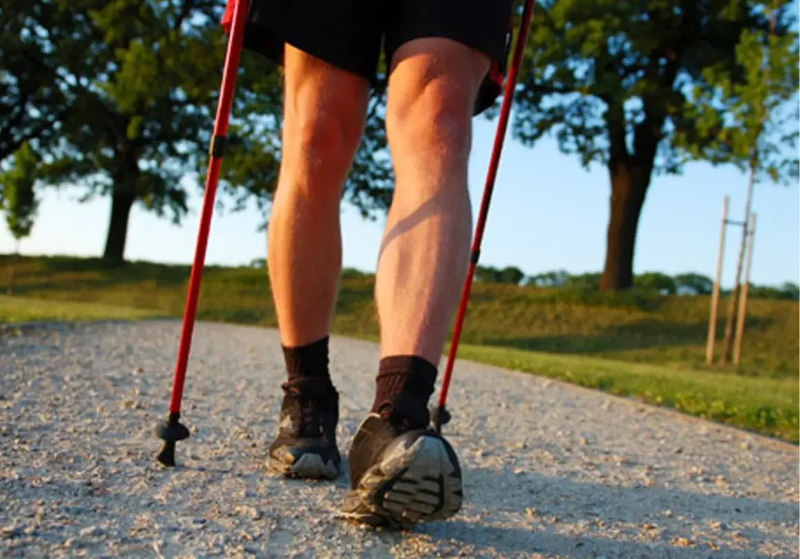 Nogi w butach i skarpetach, z kijkami nordic walking. Dowiedz się, jak prawidłowo założyć buciki na kijki nordic walking, by cieszyć się spacerem.
