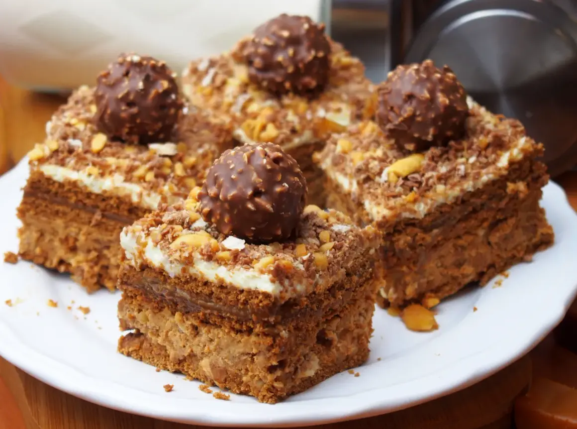 Pyszne ciasto Ferrero Rocher z kremem i orzechami, udekorowane całymi czekoladkami.