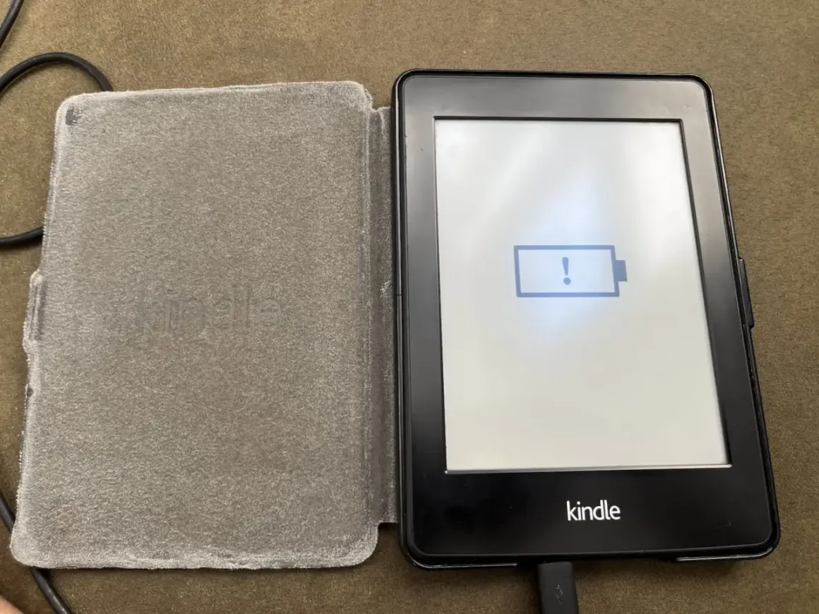 Un Kindle avec une batterie faible, prêt à être éteint. L'icône de batterie vide et le point d'exclamation indiquent qu'il est temps de le charger.