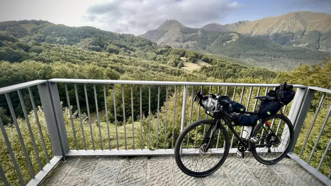 Bicicletta da cicloturismo pronta per esplorare l'Appennino Tosco Emiliano, con un panorama mozzafiato di boschi e montagne.
