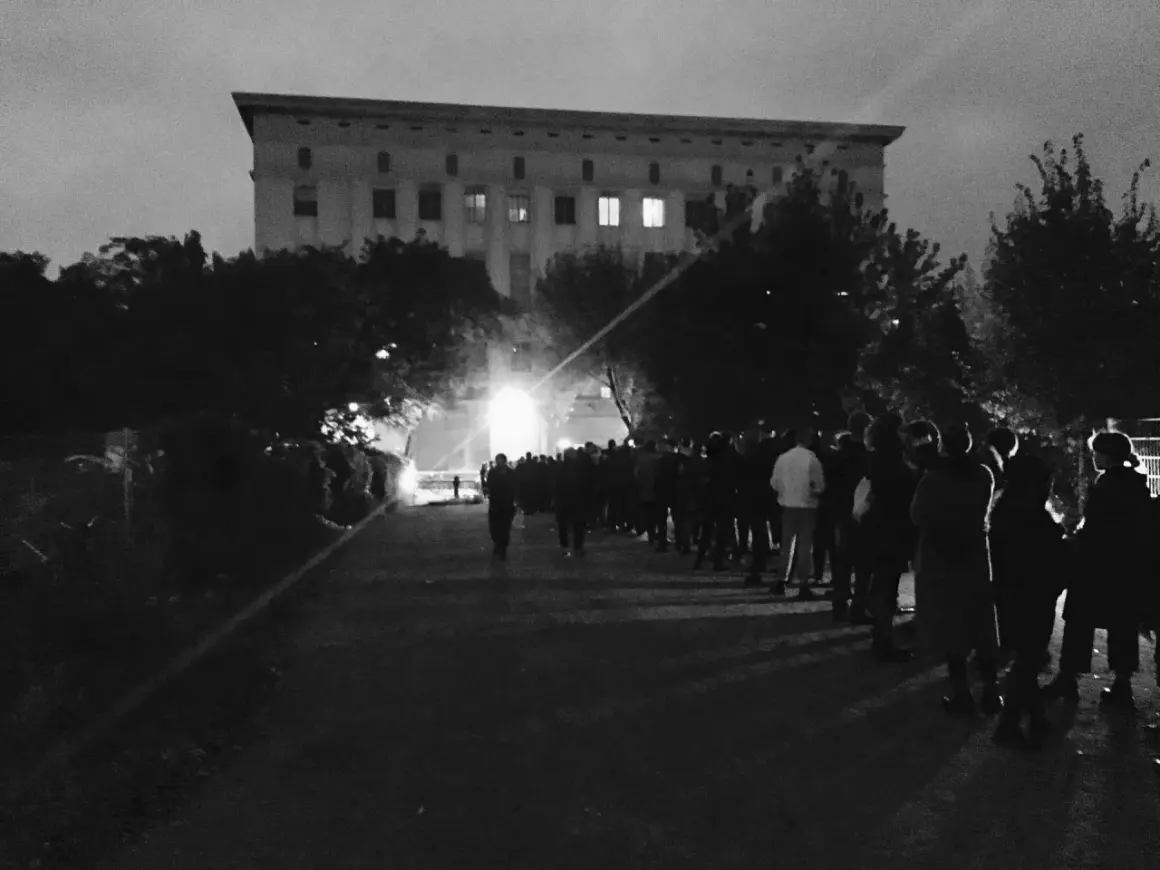 Folla in fila davanti a un imponente edificio, un iconico night club berlino, nella notte.