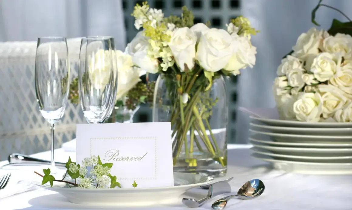 Elegancko nakryty stół z białymi różami, kieliszkami i kartą "Reserved". Idealny na przyjęcie, gdzie wedding planner cena jest kluczowa.
