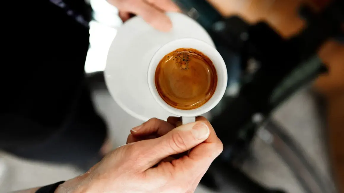 En hand håller en kopp med en perfekt dubbel espresso, med gyllene crema som lovar en intensiv smakupplevelse.