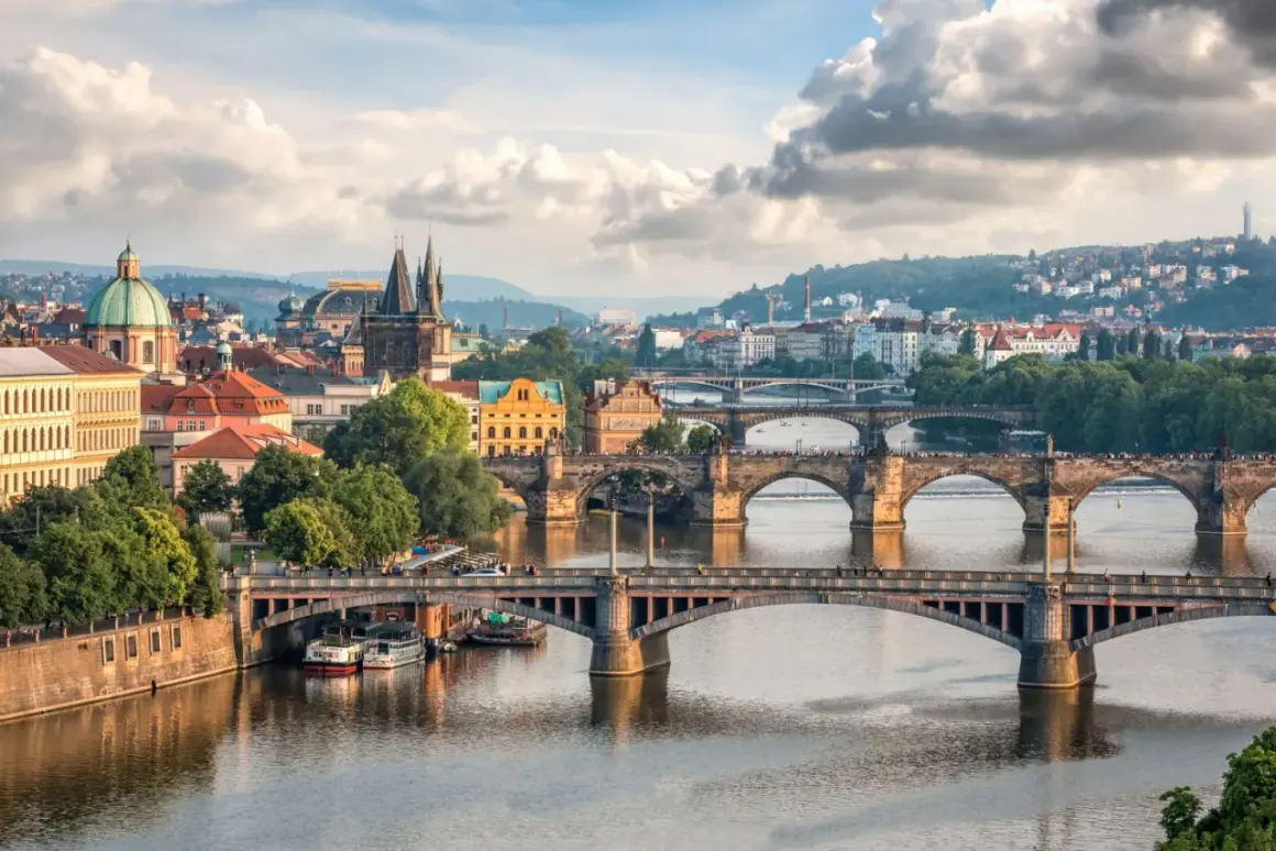 Widok na wiele mostów w Czechach, w tym Most Karola, nad Wełtawą, z praskim zamkiem i wzgórzami w tle.