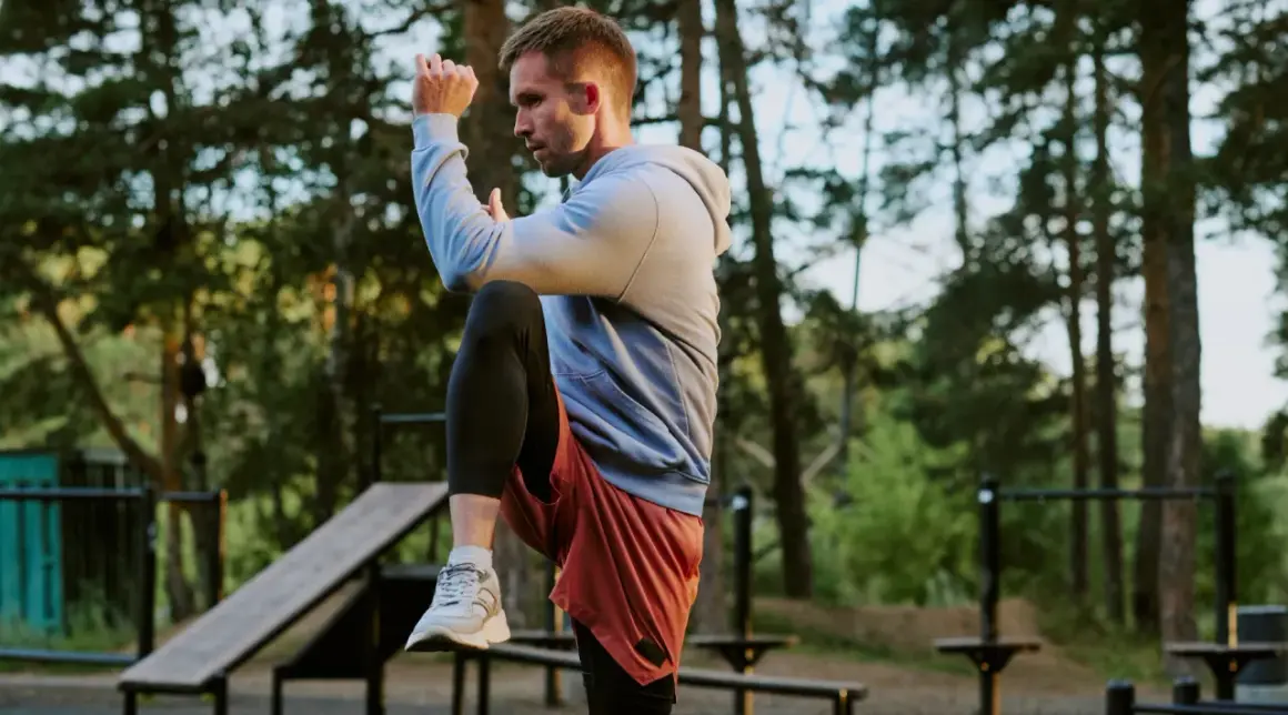 Mann im Freien beim **hit training**, hebt ein Knie, konzentriert sich auf seine Bewegung.
