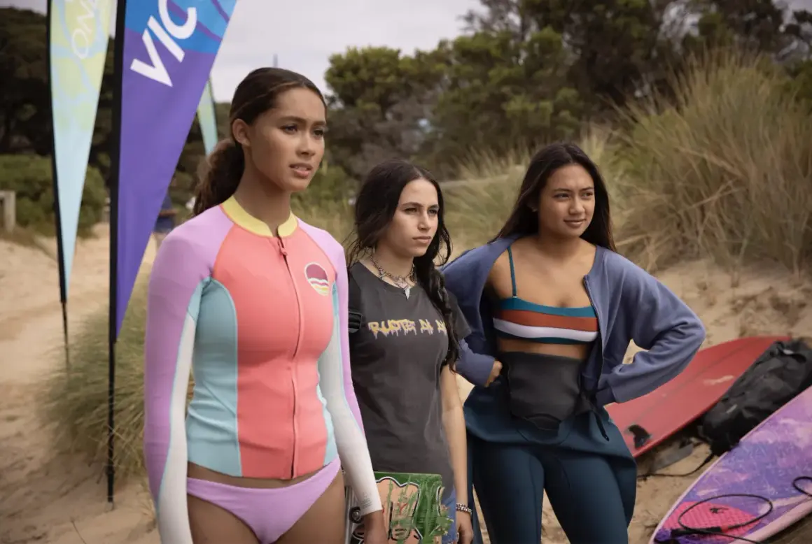 Drei junge Frauen stehen am Strand, bereit für die Wellen. Savannah La Rain und ihre Freundinnen warten auf den perfekten Surf.