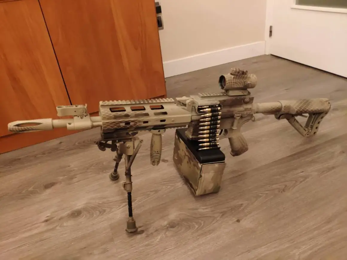 Réplica de airsoft con camuflaje personalizado. El detalle de pintar replica airsoft es impresionante, con un cargador de cinta y mira holográfica.