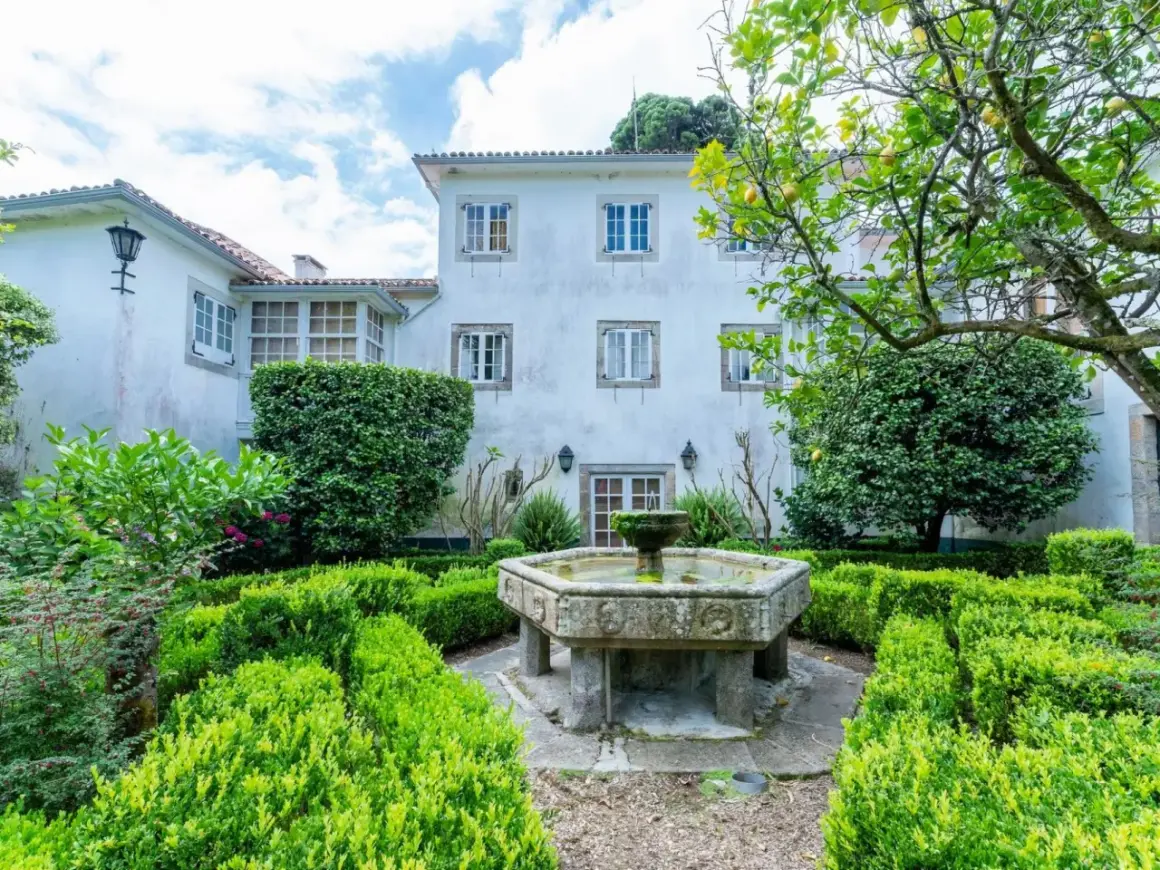 Jardín del pazo do casal con fuente de piedra y setos verdes.