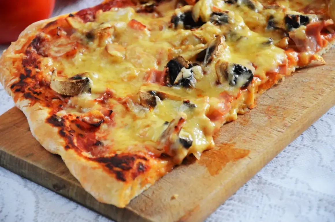 Pyszna pizza capriciosa z pieczarkami i szynką, roztopionym serem, na drewnianej desce.