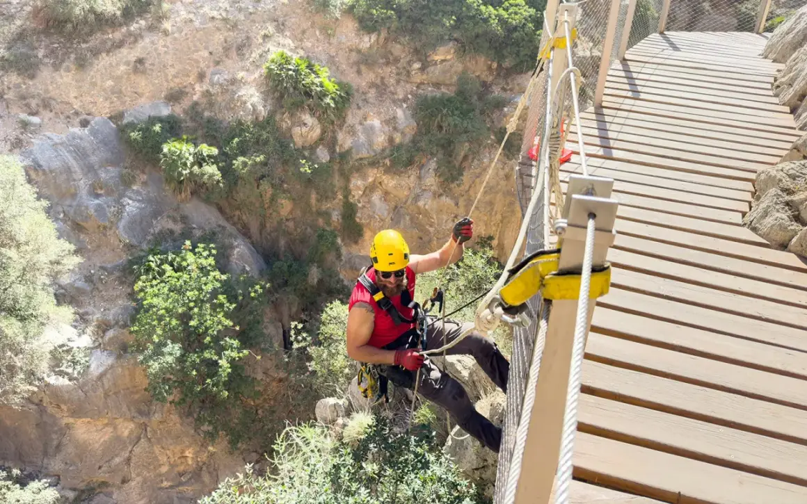 Man i gul hjälm klättrar på en hängbro längs Caminito del Rey, en dramatisk klippstig.