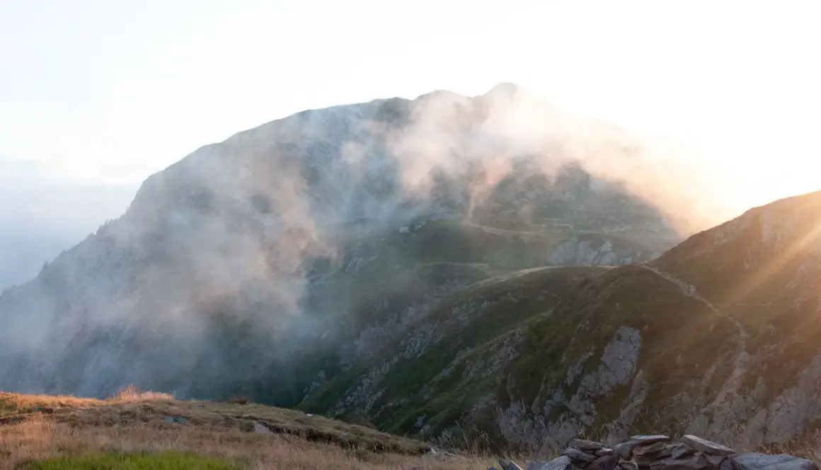 Sentier brumeux sur les hauteurs, un aperçu du tour du Mont-Blanc en 3 jours. Lumière dorée filtrant à travers les nuages.