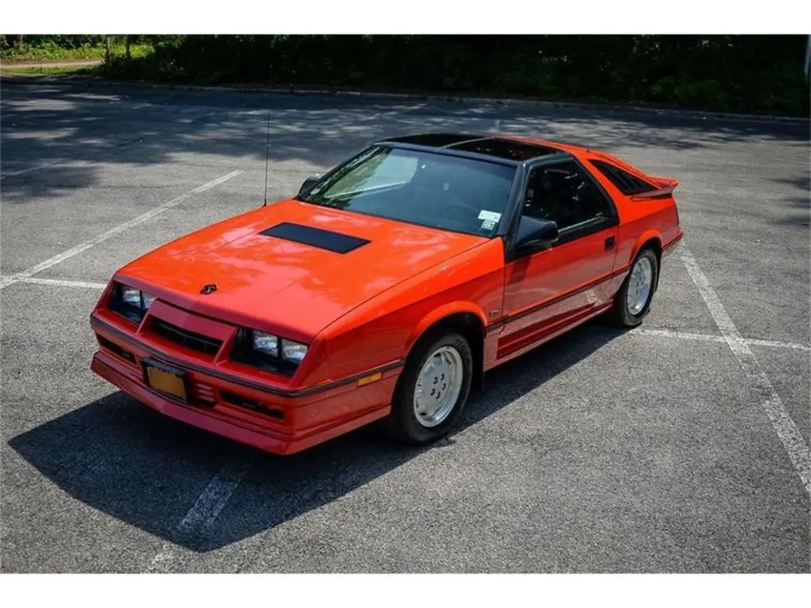 Pomarańczowy Dodge Daytona z czarnym dachem i spojlerem na parkingu.