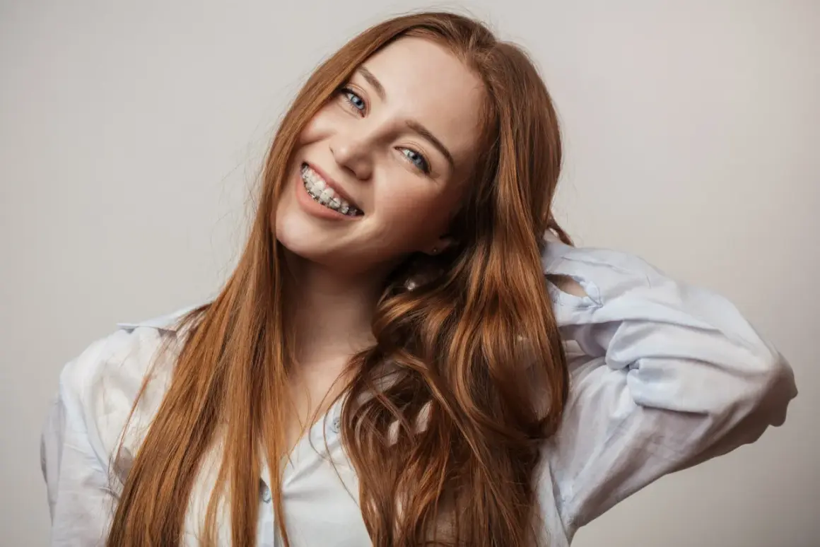 Uśmiechnięta rudowłosa dziewczyna z aparatem na zębach, który koryguje tyłozgryz, zmieniając rysy twarzy.