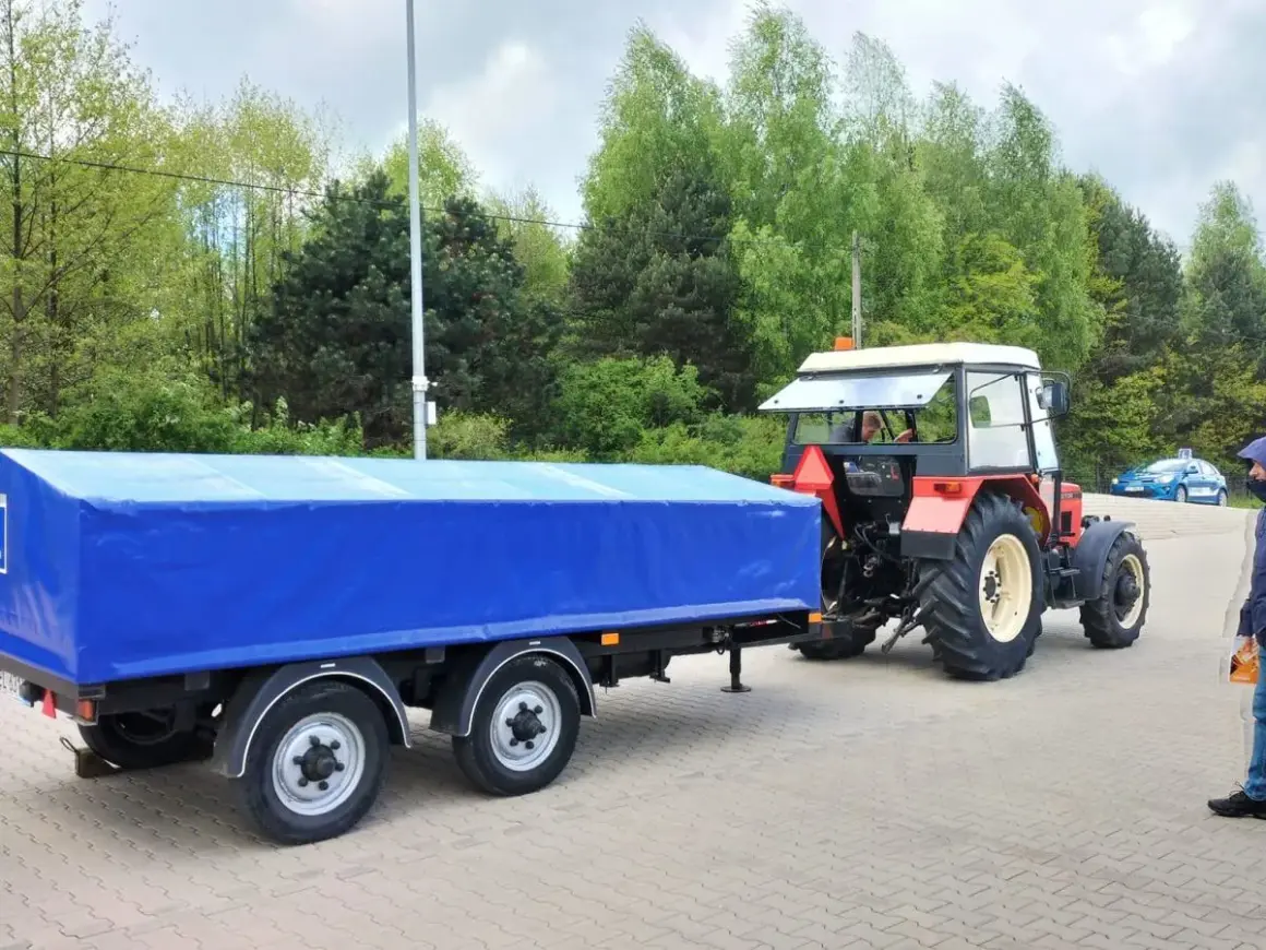 Czerwony traktor z niebieską plandeką na przyczepie. Zastanawiasz się, prawo jazdy kat T od ilu lat?