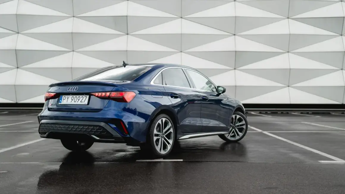 Eleganckie, nowe Audi A3 w kolorze granatowym prezentuje się stylowo na tle nowoczesnej architektury.