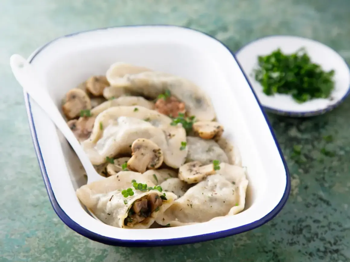 Pyszne pierogi z pieczarkami i serem, posypane natką pietruszki, w białej misce z niebieską obwódką.