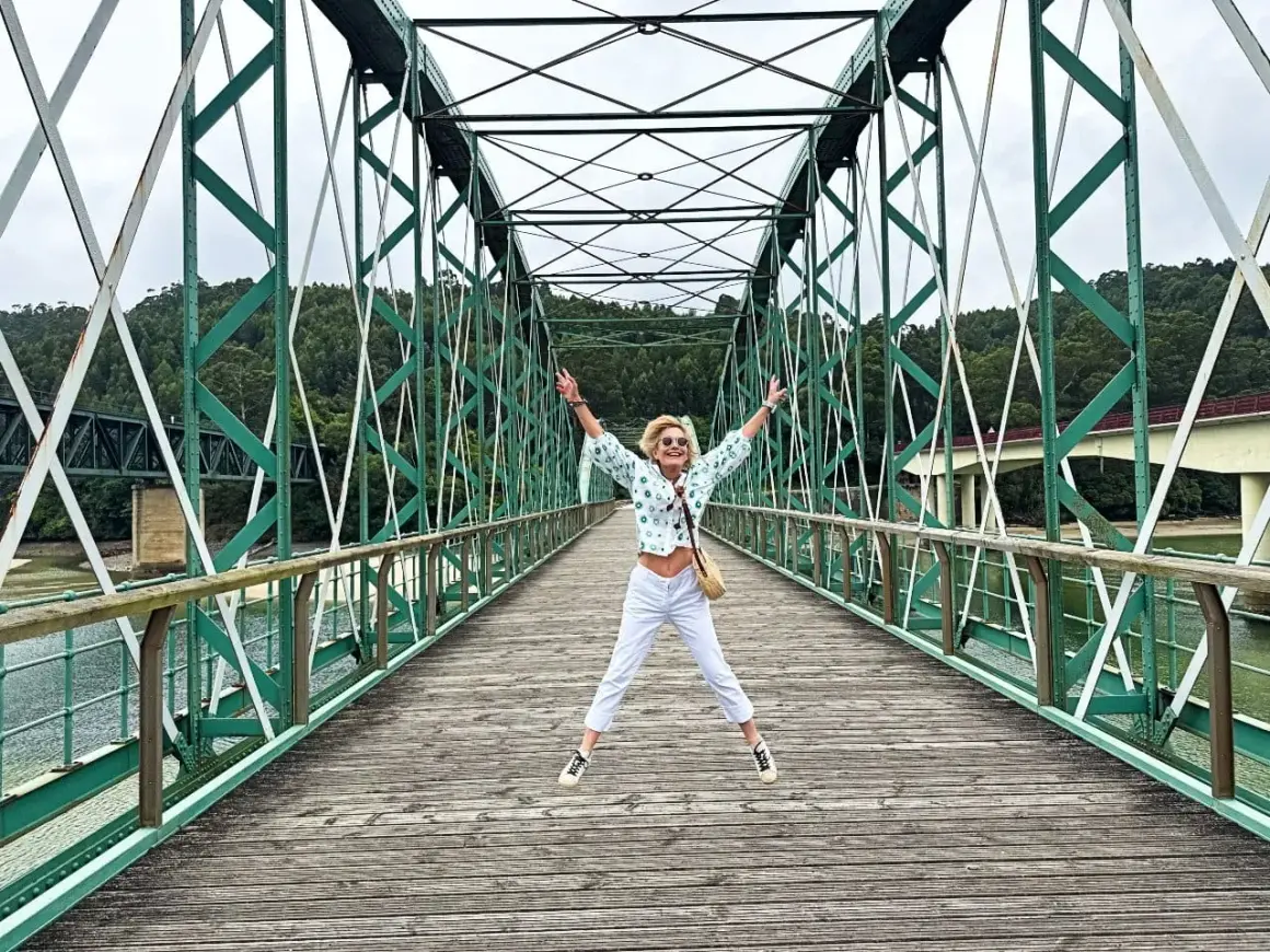 Mujer salta de alegría en un puente verde, disfrutando de las vistas. ¡Un lugar genial que ver en O Vicedo!