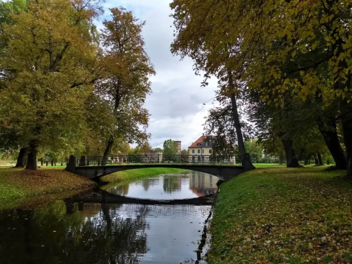 Jesienny park w Choroszczy z mostkiem nad kanałem i pałacem w tle.