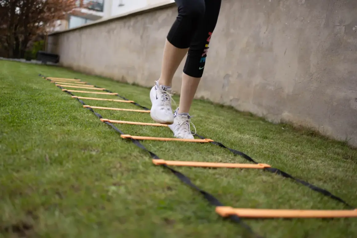 Une personne effectue un exercice lombaire sur une échelle d'agilité dans l'herbe.