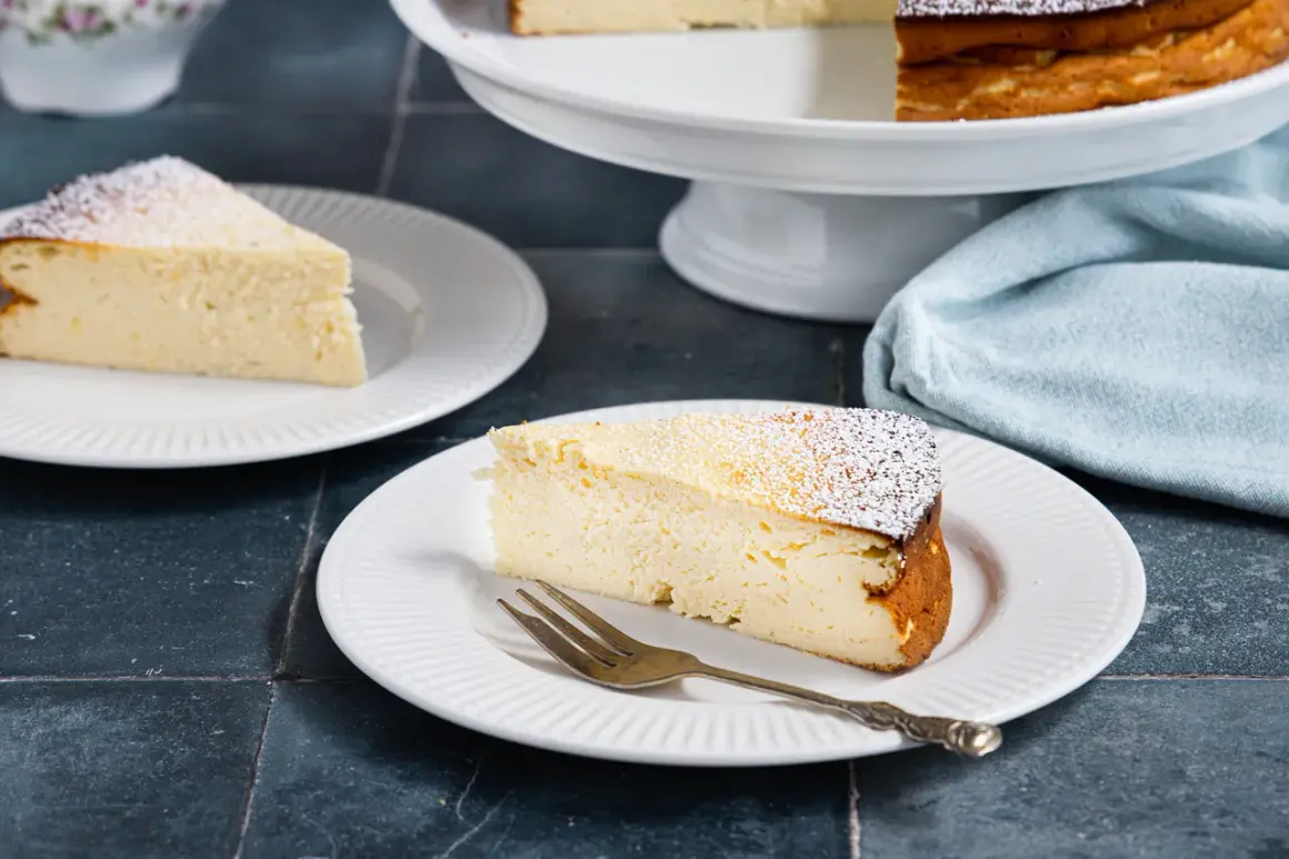 Ein Stück cremiger Quarkkuchen ohne Boden, bestäubt mit Puderzucker, wartet auf dem Teller.