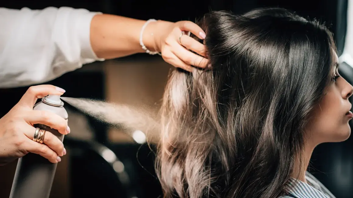Hårstylist fixar en elegant edgar hairstyle med hårspray.
