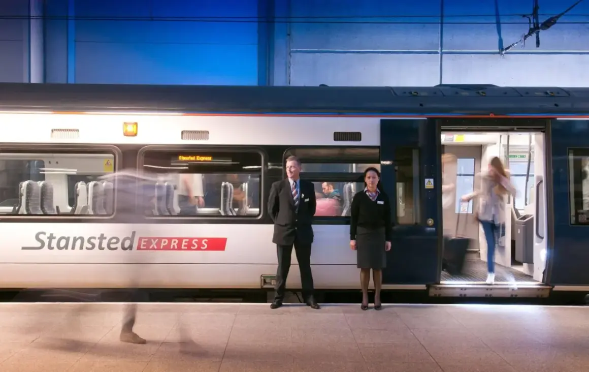 Pociąg Stansted Express na stacji. Pracownicy obsługi i pasażerowie wsiadają i wysiadają. Szybki transport z lotniska do centrum Londynu.
