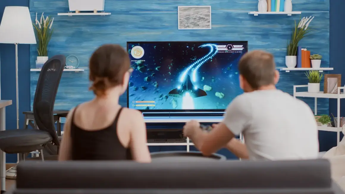 Para grająca w grę kosmiczną na dużym telewizorze.
