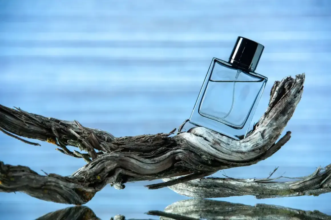 Szklana butelka perfum na dryfującym drewnie, w tle błękitna woda. Czy to zapach ambra co to?