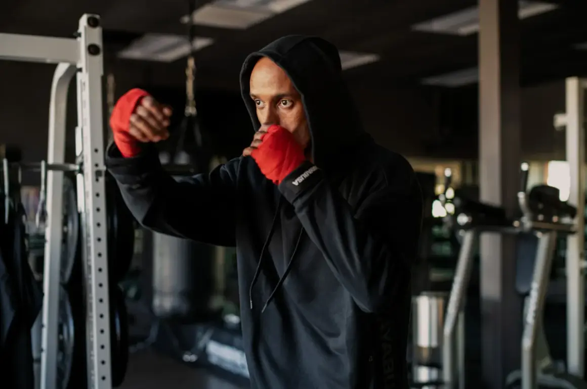 A man in a black hoodie with red hand wraps practices shadow boxing, his intense gaze reflecting the mental discipline of the sport.