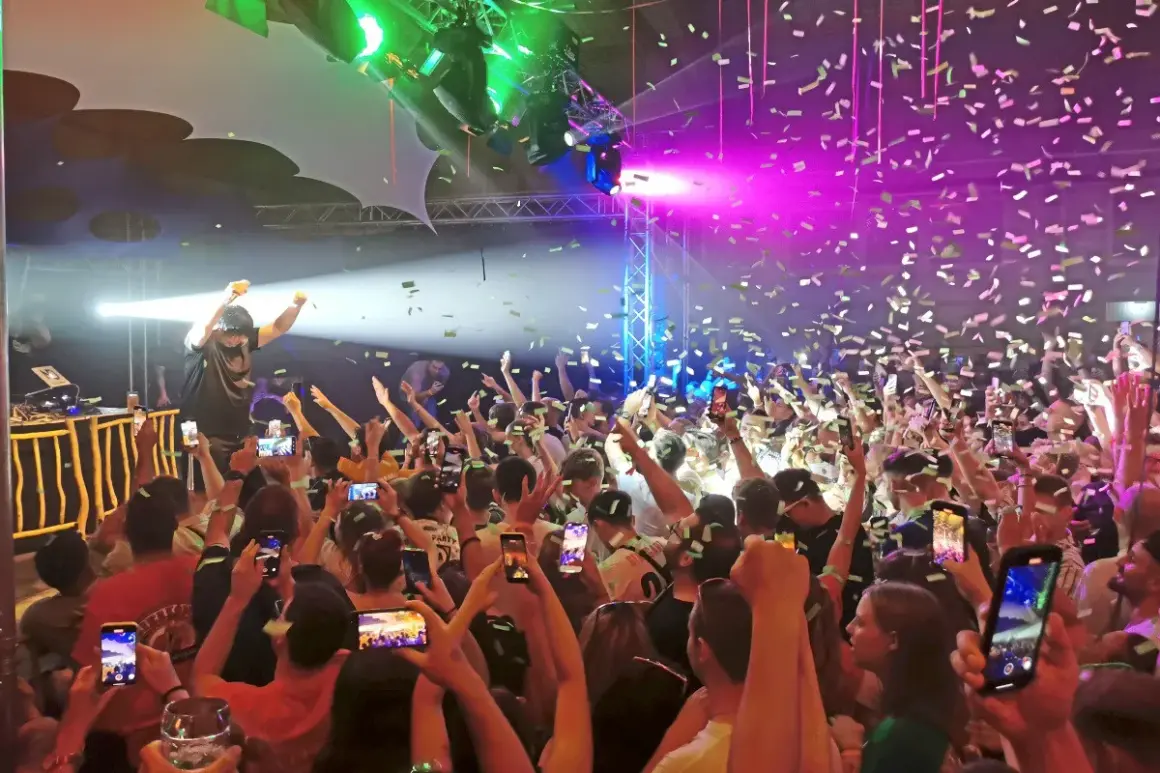 Konfetti regnet auf eine jubelnde Menge bei einem Konzert. Ein DJ steht auf der Bühne, während die Leute ihre Handys hochhalten, um den Moment beim Altdorfer Wasen festzuhalten.