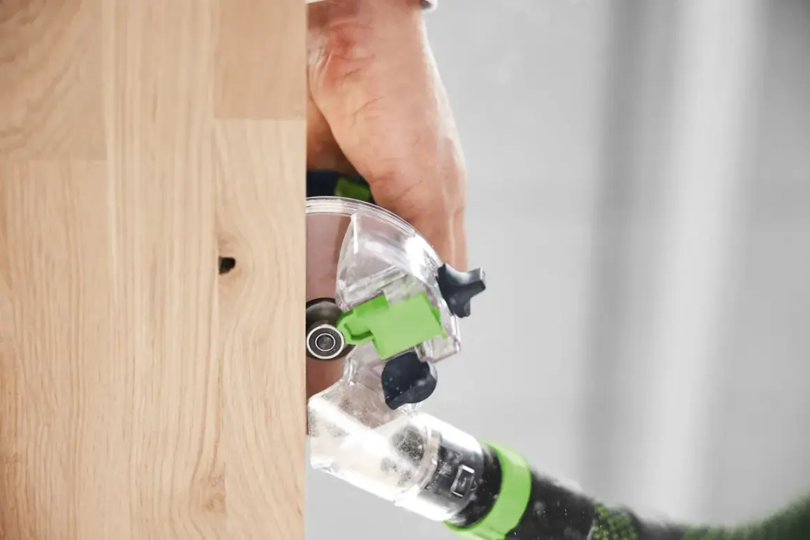 Main d'un artisan utilisant la défonceuse Festool OFK 500 pour travailler le bois avec précision.
