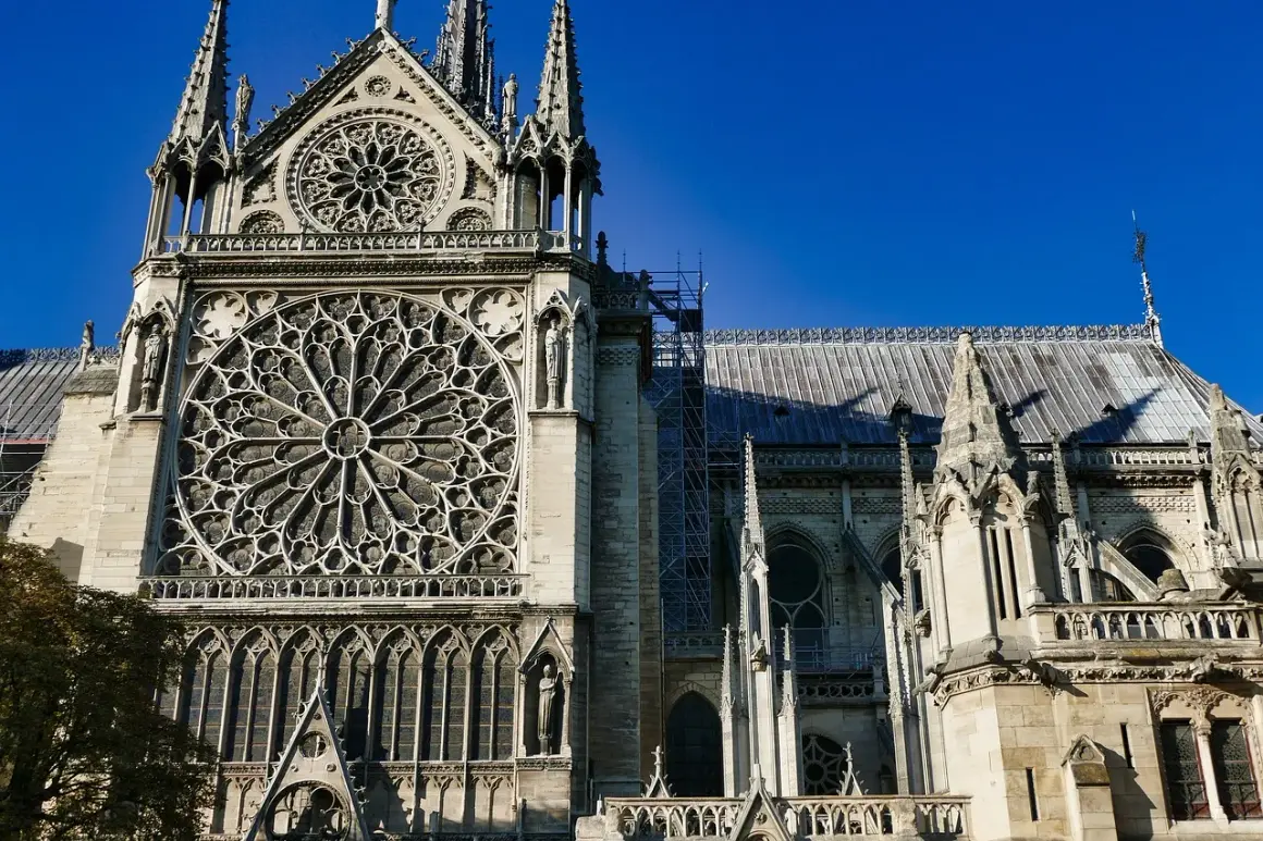 Majestatyczna katedra Notre Dame w Paryżu z imponującą rozetą i gotyckimi detalami, na tle błękitnego nieba.