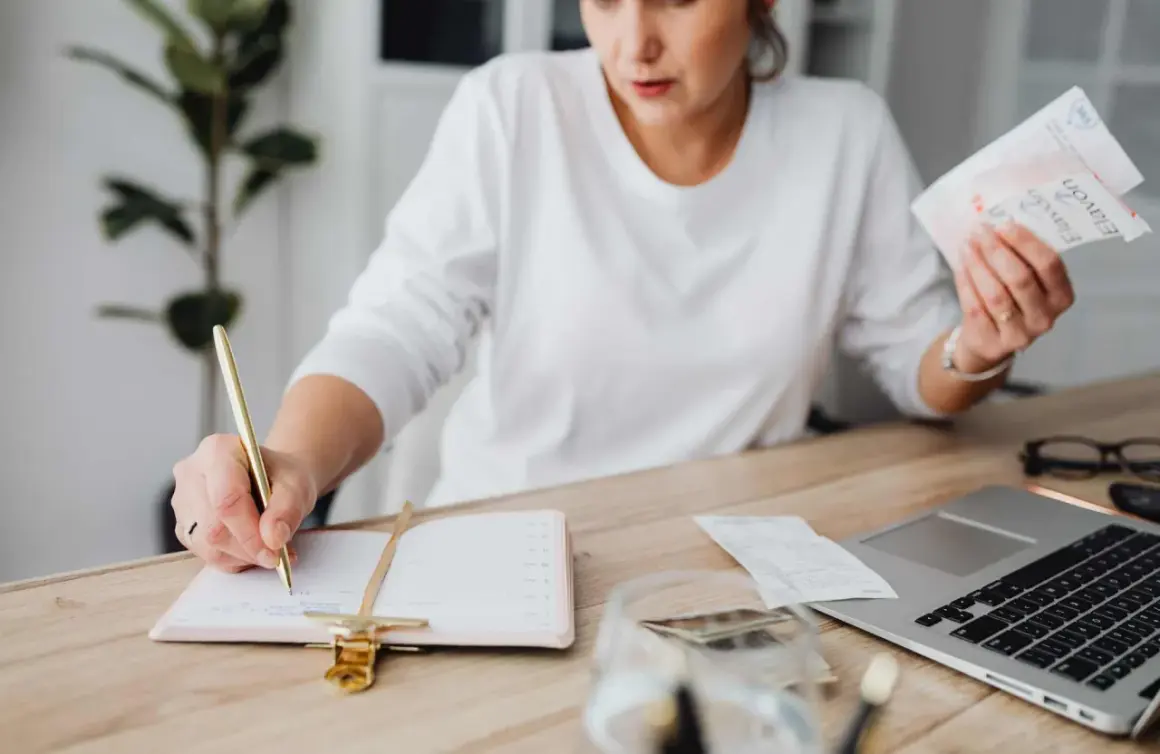 Mujer revisa facturas y escribe en agenda. El heredero no paga gastos vivienda, pero ella organiza las finanzas.