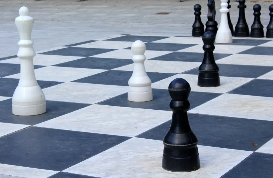 Duże figury szachowe na planszy. Biała królowa i czarne pionki czekają na ruch, jak zbijają pionki w szachach.