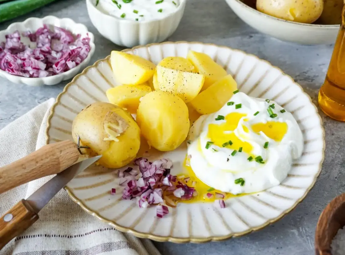 Kartoffeln mit Quark, garniert mit Schnittlauch und verfeinert mit Öl. Dazu gibt es gehackte rote Zwiebeln und ein Messer zum Schälen.