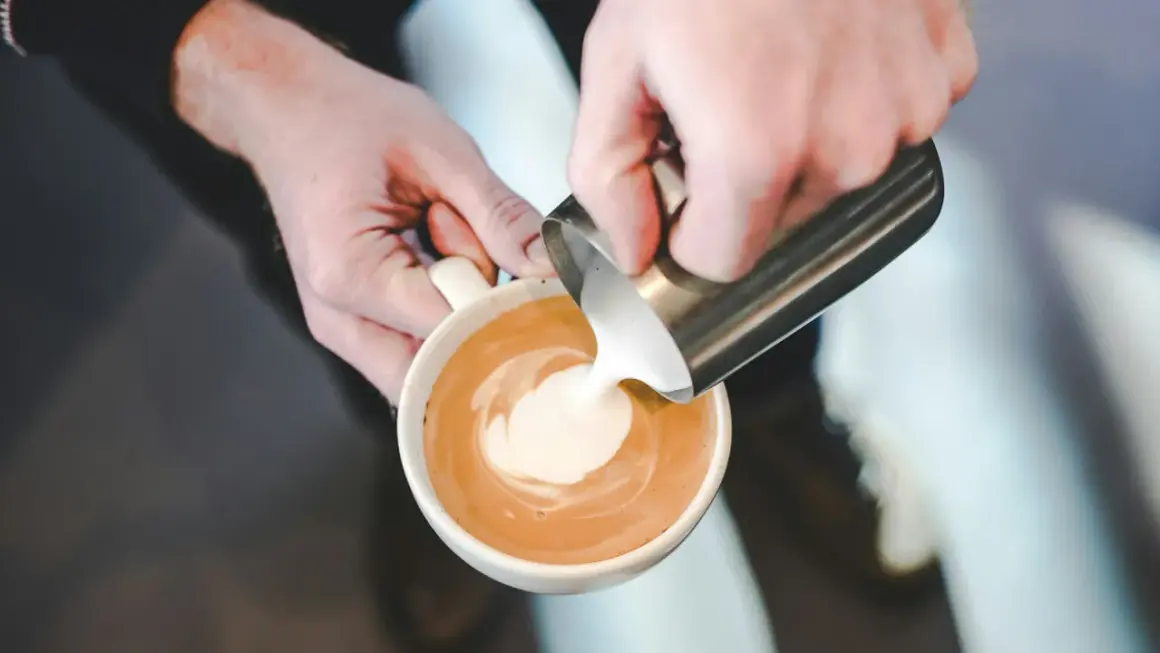 Barista versa latte art, mostrando come fare la schiuma al latte per un cappuccino perfetto.
