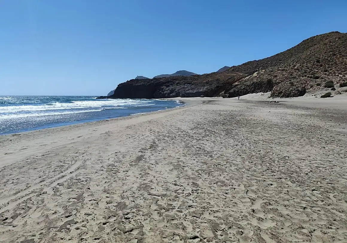 Arena dorada y mar azul en la almerimar playa, con montañas rocosas al fondo bajo un cielo despejado.