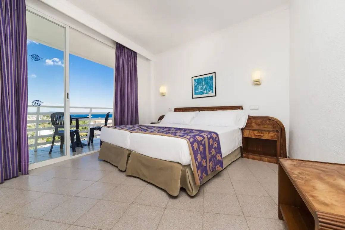 Pokój w hotelu Globales Palmanova Palace z widokiem na morze. Dwa łóżka, fioletowe zasłony i balkon.