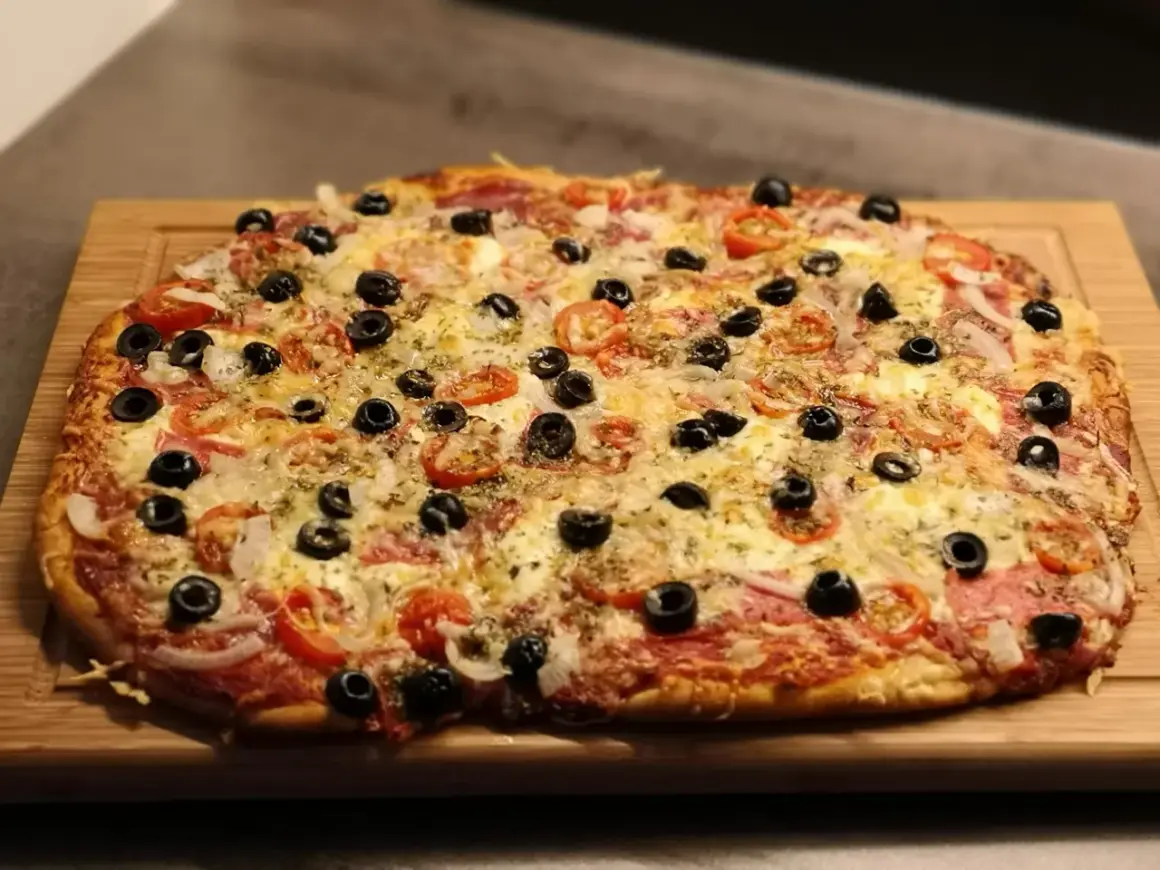 Frisch gebackene Pizza mit Tomaten, Oliven und Käse auf einem Holzbrett. Der Pizzateig wurde im Thermomix zubereitet.