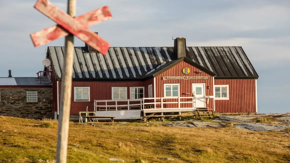STF Blåhammaren Fjällstation, en röd fjällstuga med vita detaljer, välkomnar vandrare i ett kargt landskap.