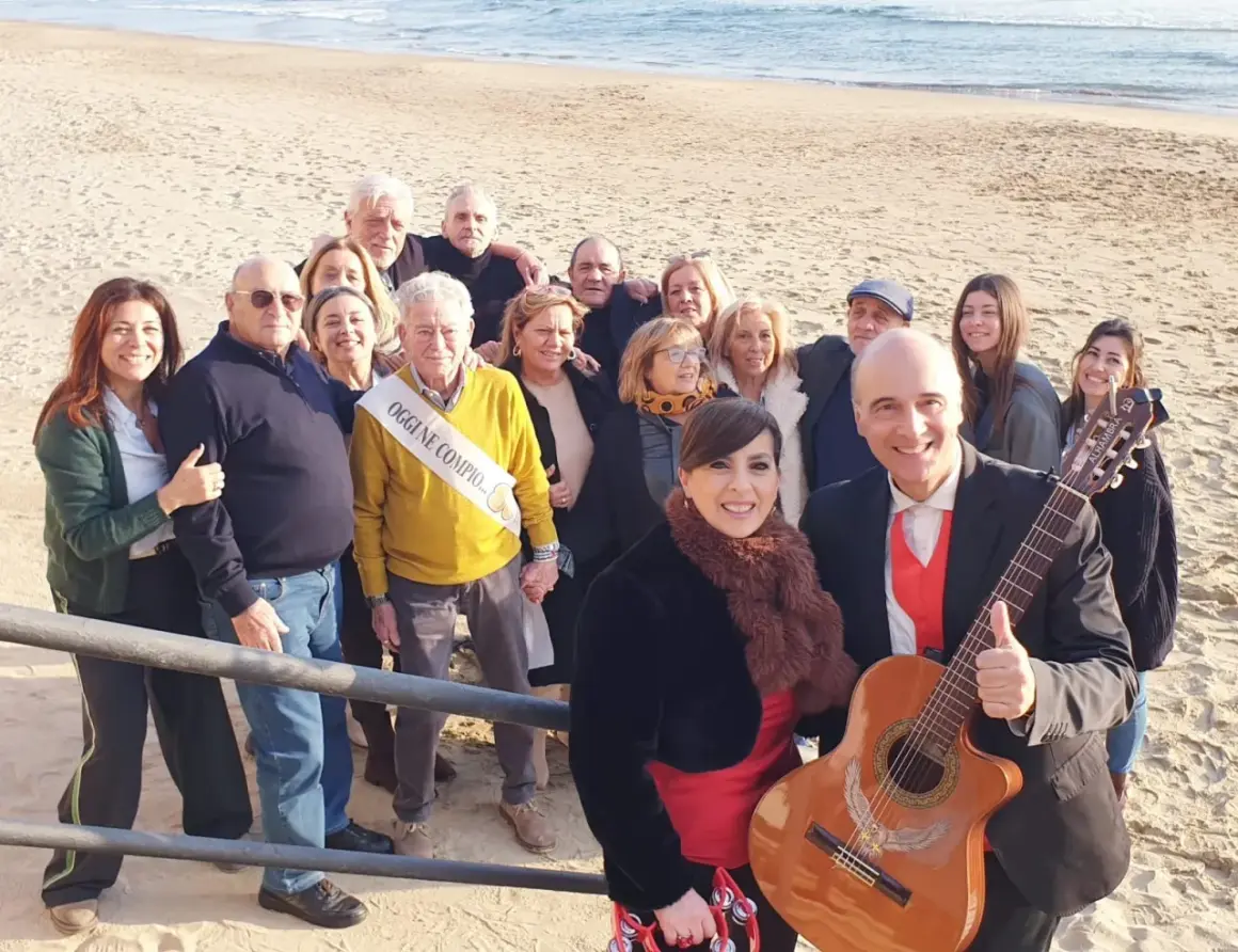 Famiglia riunita sulla spiaggia per festeggiare un compleanno con una "posteggia napoletana" e chitarra.