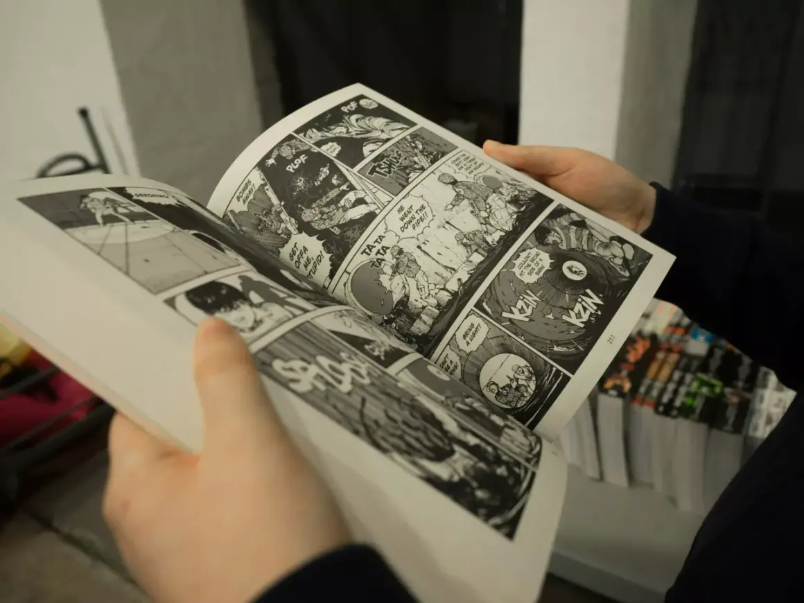 Des mains tiennent un manga ouvert, révélant des cases de bande dessinée pleines d'action. Apprendre comment lire un manga est facile avec ces images dynamiques.